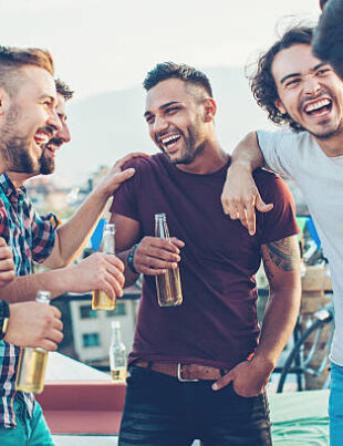 Multi-ethnic group of young men chatting and drinking beer on a rooftop party.